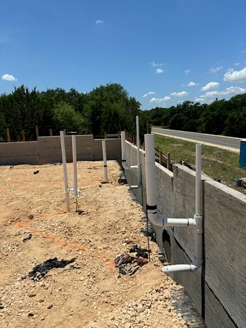 Commercial plumbing installation with concrete foundation, metal posts, and PVC piping on cleared lot