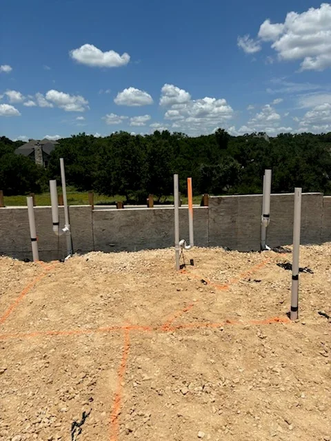 PVC utility posts installed in concrete foundation with cleared construction site and tree line background